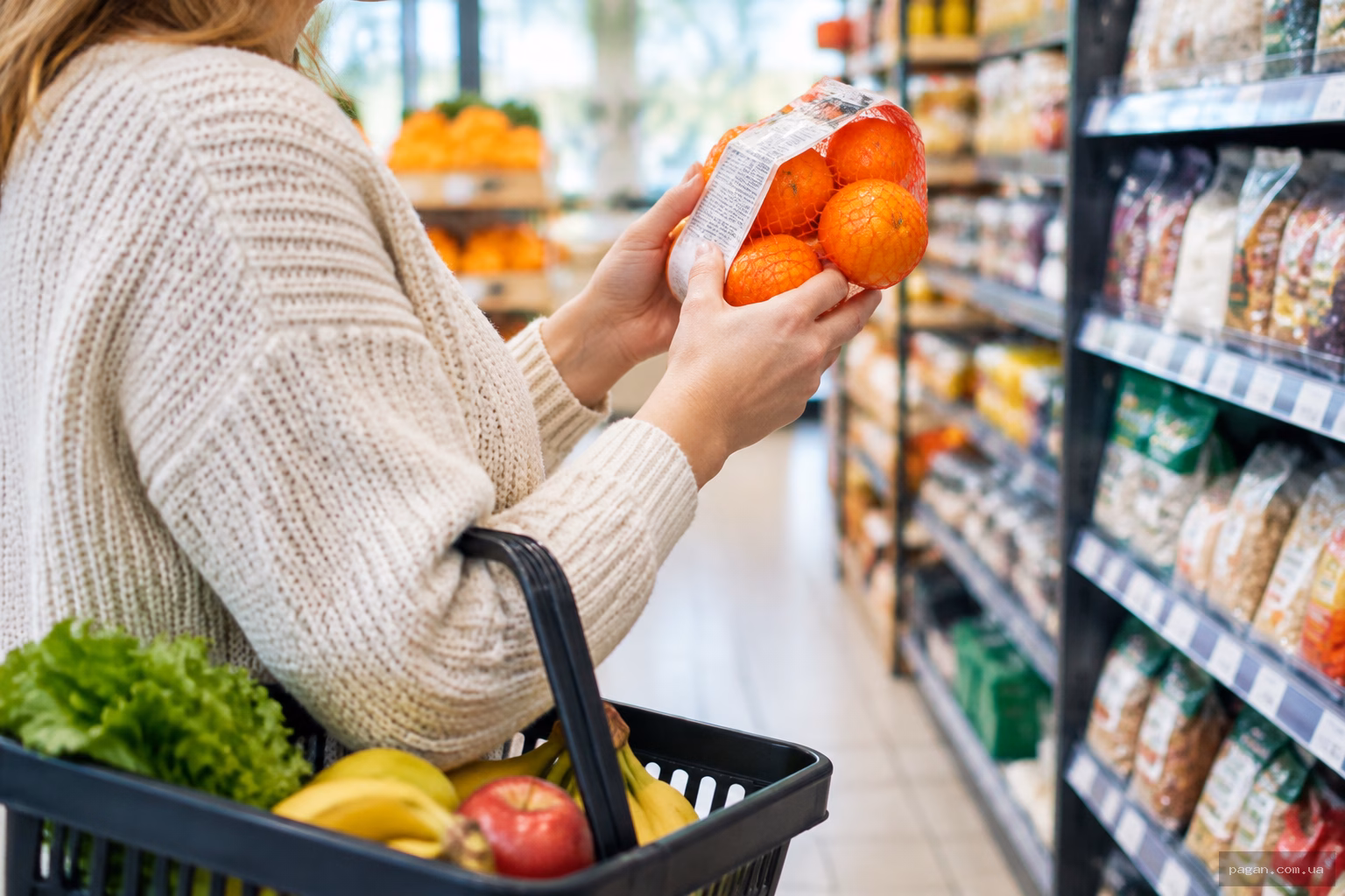 Жінка читає склад продукту на етикетці в магазині, тримаючи кошик із фруктами