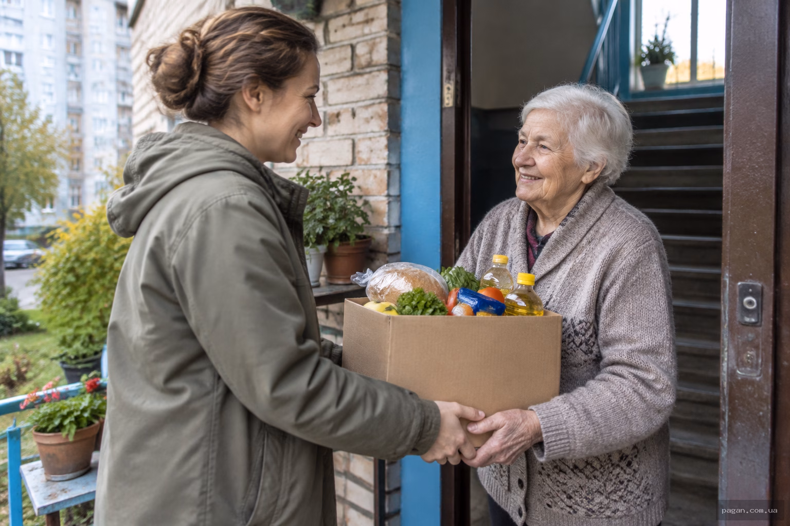 Волонтер передає продуктовий набір літньому сусідові біля дверей квартири