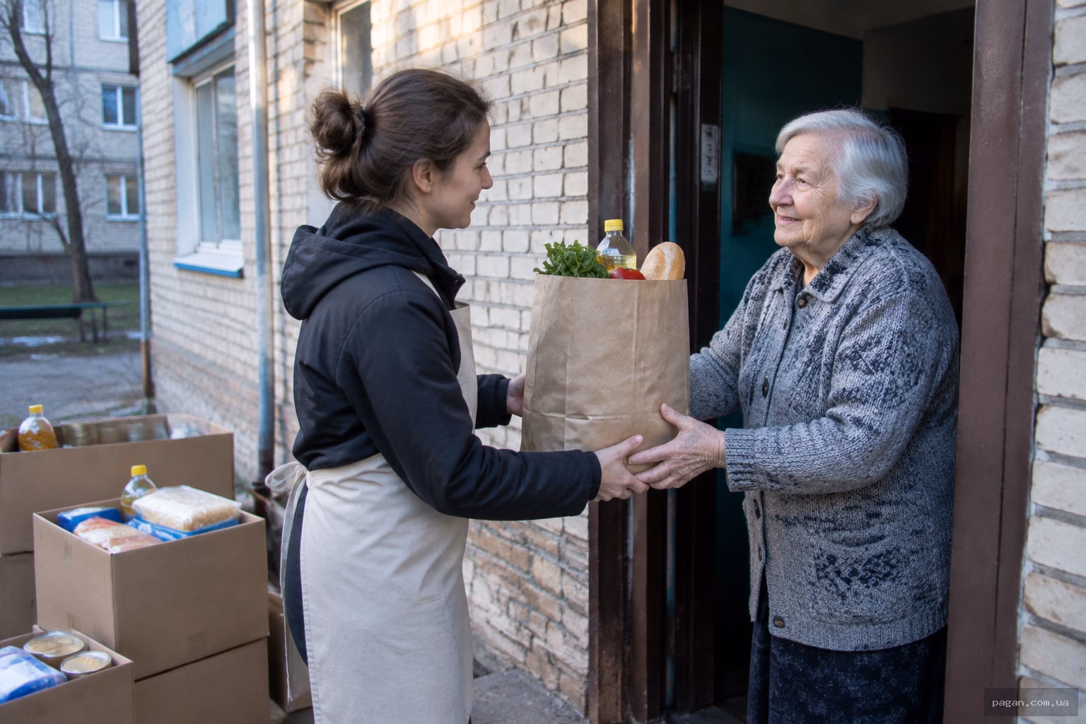 Волонтер передає пакунок з продуктами літній жінці біля під’їзду