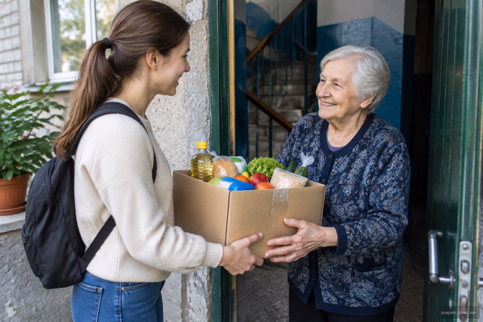 Волонтерка передає продуктовий набір літній сусідці біля дверей помешкання