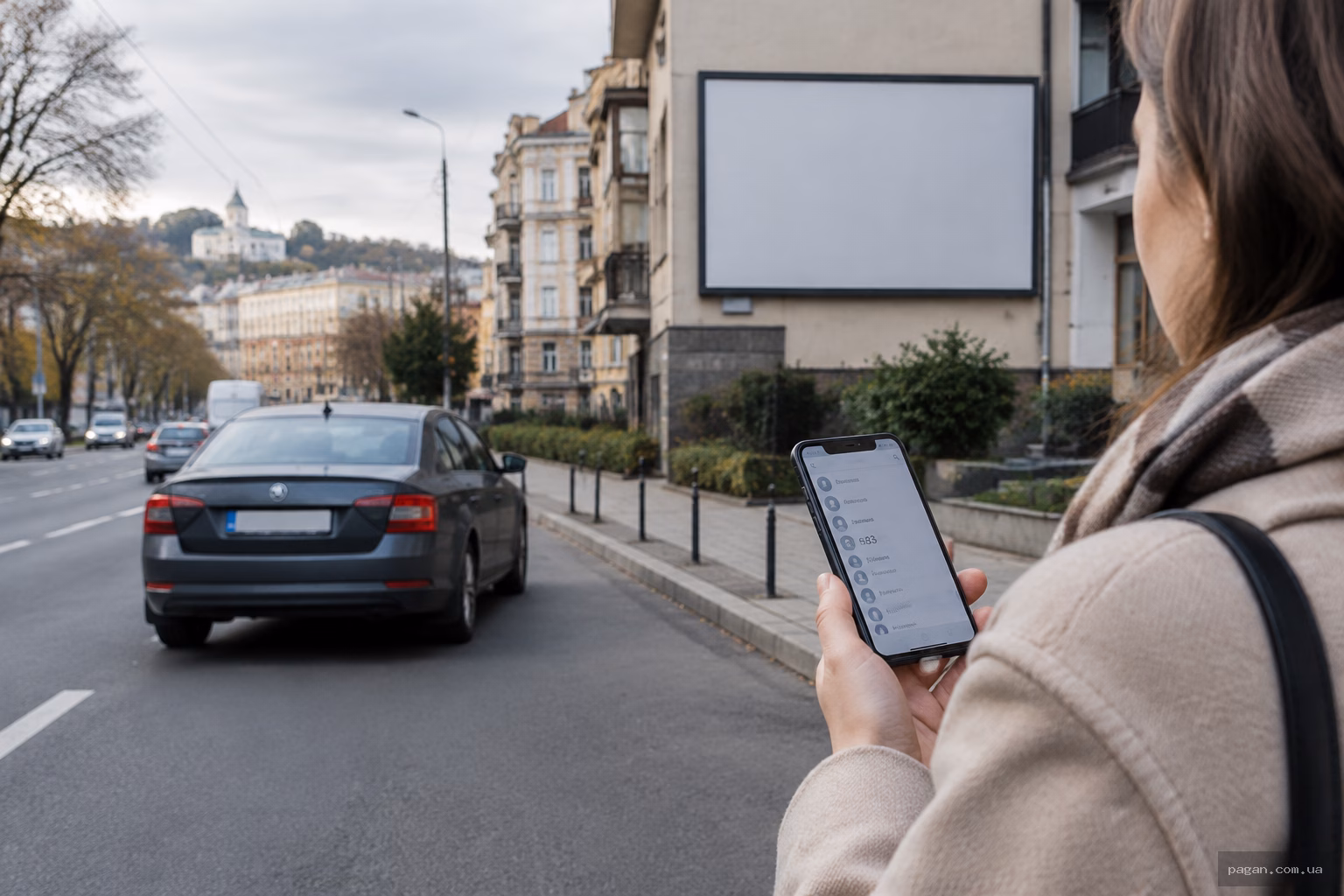 Вулична сцена в українському місті з автомобілем попереду та рекламним щитом