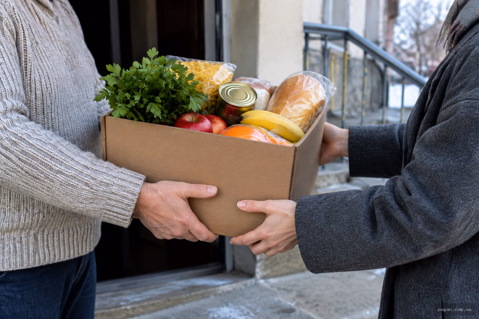 Дві людини передають коробку з продуктами біля дверей