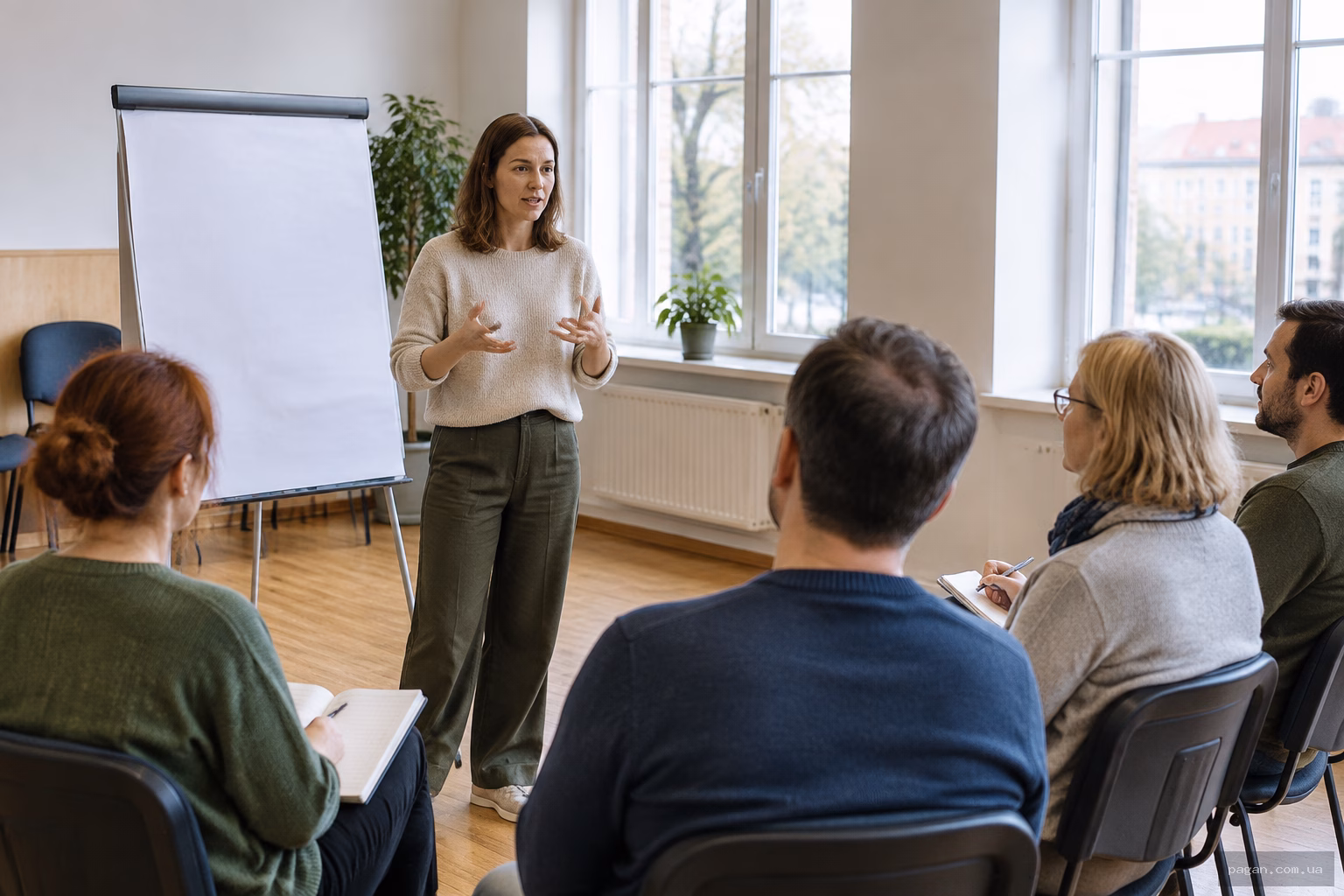 Жінка проводить заняття для невеликої групи дорослих у світлій залі, ділячись досвідом